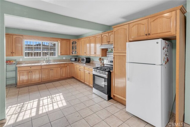 kitchen with light brown cabinets, white fridge, sink, light tile patterned floors, and stainless steel range with gas stovetop