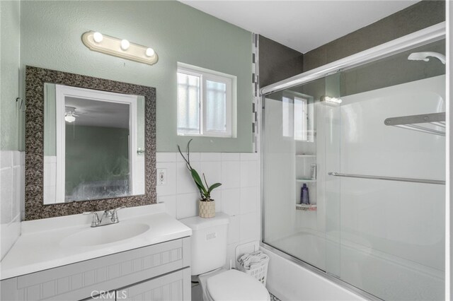 full bathroom with bath / shower combo with glass door, toilet, vanity, and tile walls