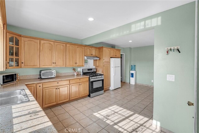 kitchen featuring white fridge, stainless steel gas range oven, light brown cabinets, light tile patterned flooring, and sink