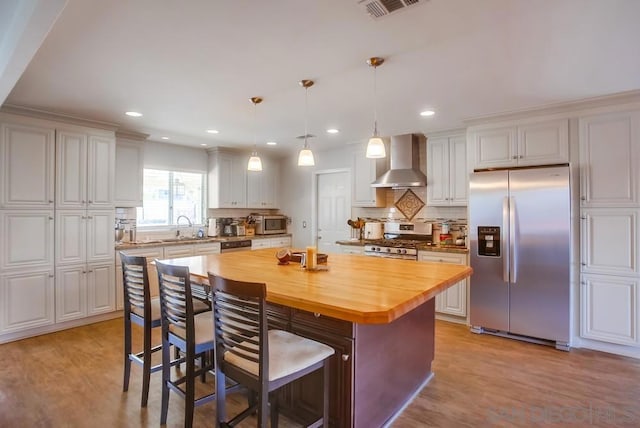 kitchen featuring hanging light fixtures, appliances with stainless steel finishes, wall chimney exhaust hood, and white cabinetry