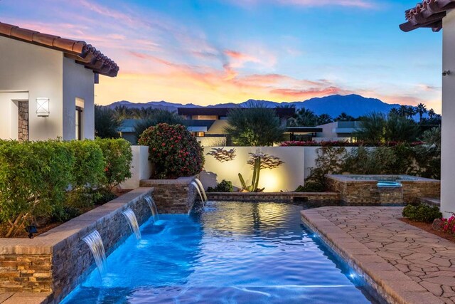 pool at dusk with pool water feature, a mountain view, and an in ground hot tub