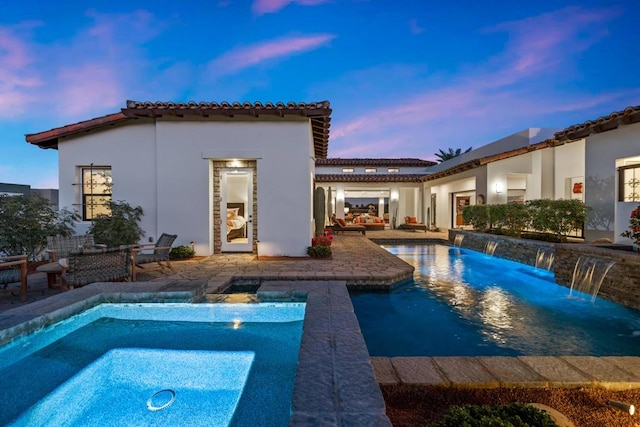 pool at dusk with an in ground hot tub, pool water feature, and a patio area