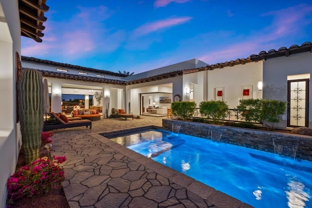 pool at dusk with a patio, an outdoor hangout area, and pool water feature