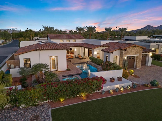 back house at dusk featuring a garage, a fenced in pool, a patio, and a mountain view