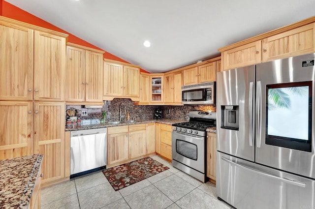 kitchen featuring appliances with stainless steel finishes, lofted ceiling, light brown cabinets, sink, and light stone counters