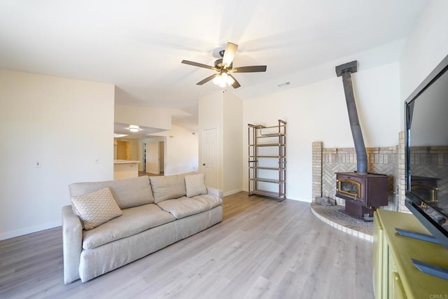 living room featuring ceiling fan, light hardwood / wood-style floors, and a wood stove