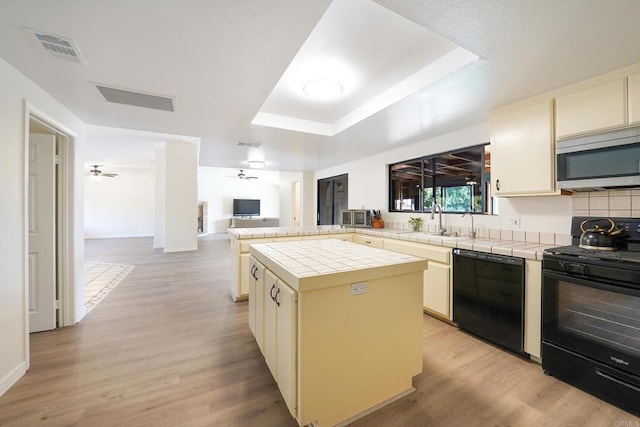 kitchen featuring ceiling fan, a center island, black appliances, tile countertops, and light wood-type flooring