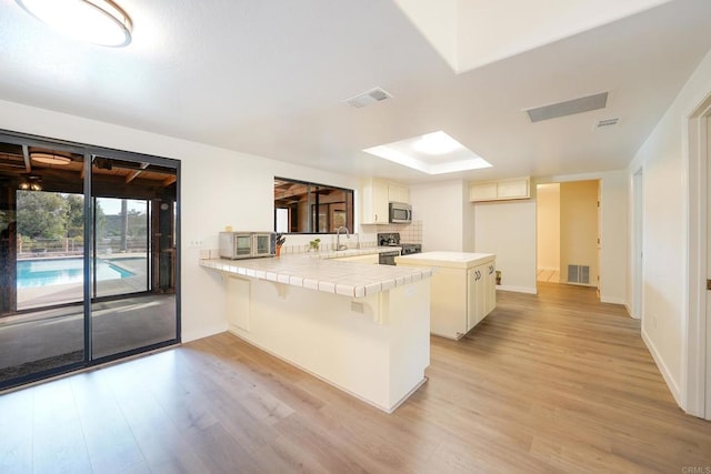 kitchen featuring a breakfast bar, white cabinetry, stainless steel appliances, tile counters, and kitchen peninsula