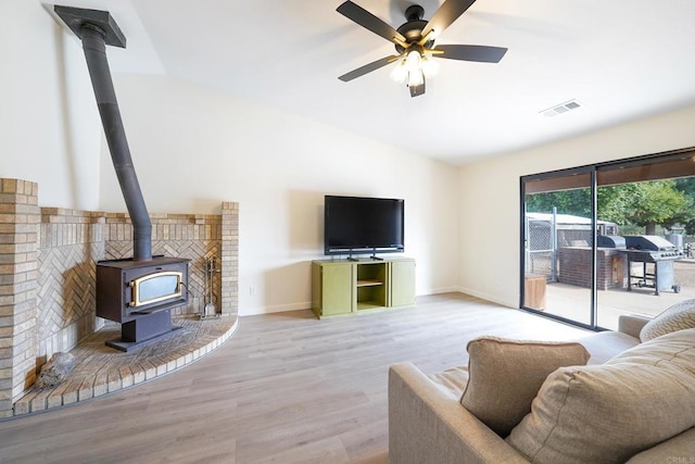 living room with light hardwood / wood-style flooring, vaulted ceiling, ceiling fan, and a wood stove