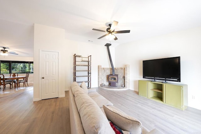 living room with wood-type flooring, a wood stove, and ceiling fan