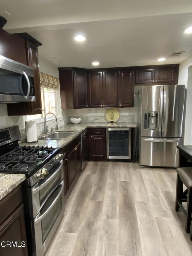 kitchen with beverage cooler, appliances with stainless steel finishes, sink, light stone counters, and light hardwood / wood-style flooring