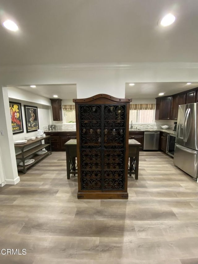 kitchen with dark brown cabinetry, appliances with stainless steel finishes, crown molding, and light wood-type flooring