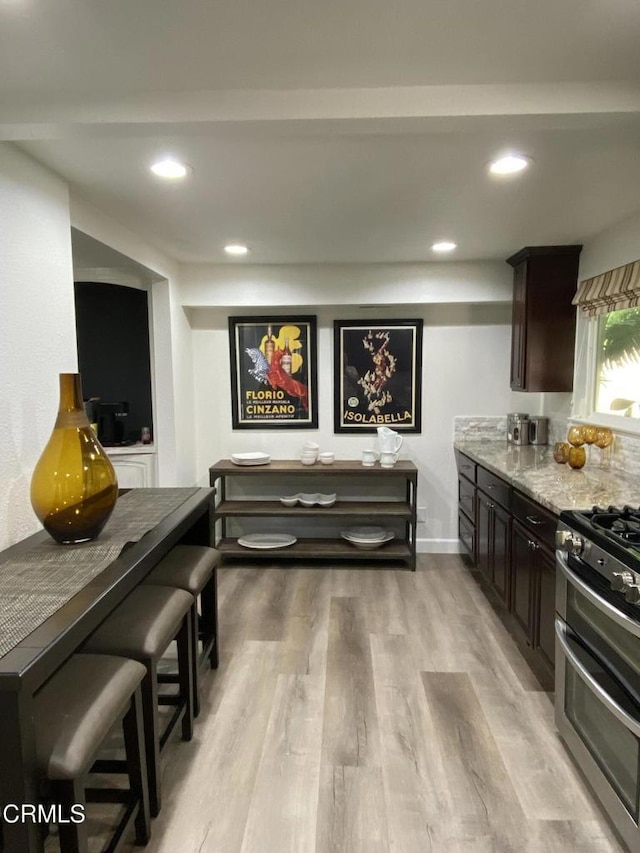 kitchen with light hardwood / wood-style flooring, dark brown cabinetry, a breakfast bar area, stainless steel gas stove, and light stone counters