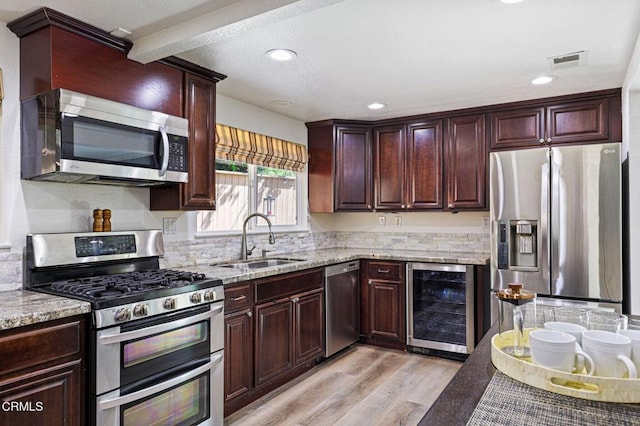 kitchen featuring visible vents, light wood-style flooring, a sink, wine cooler, and appliances with stainless steel finishes