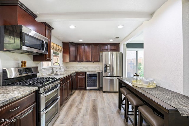 kitchen featuring light wood-type flooring, a sink, light stone counters, wine cooler, and appliances with stainless steel finishes