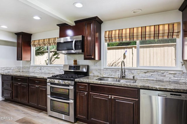 kitchen featuring decorative backsplash, light stone countertops, appliances with stainless steel finishes, and a sink