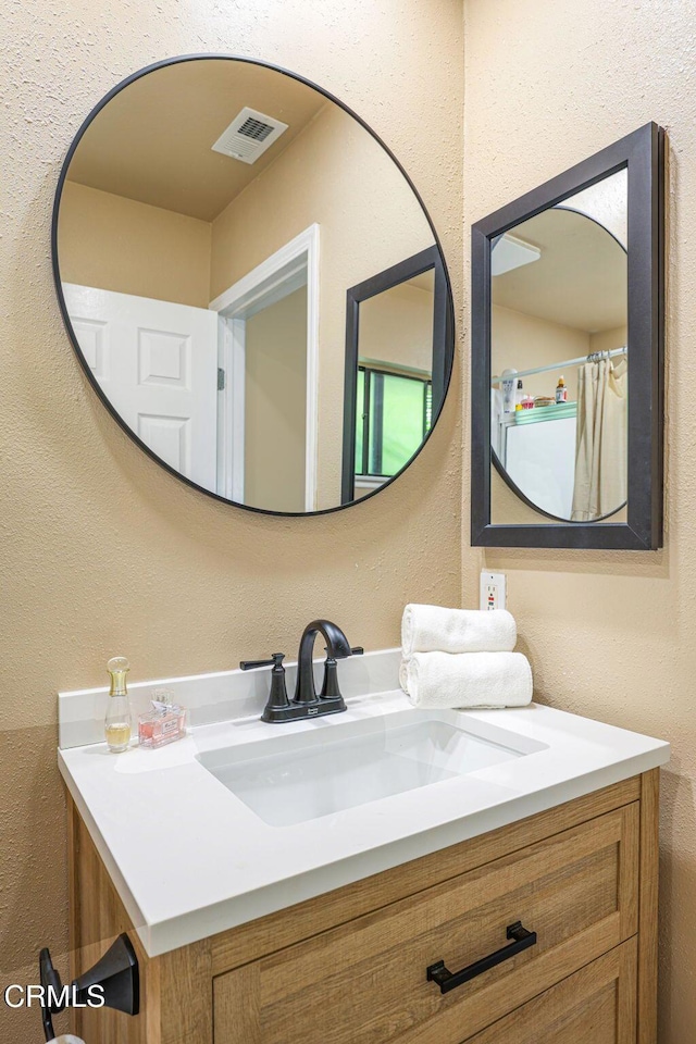 full bathroom featuring vanity, a textured wall, and visible vents