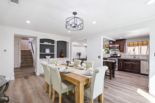 dining area with visible vents, crown molding, stairway, light wood-style flooring, and an inviting chandelier