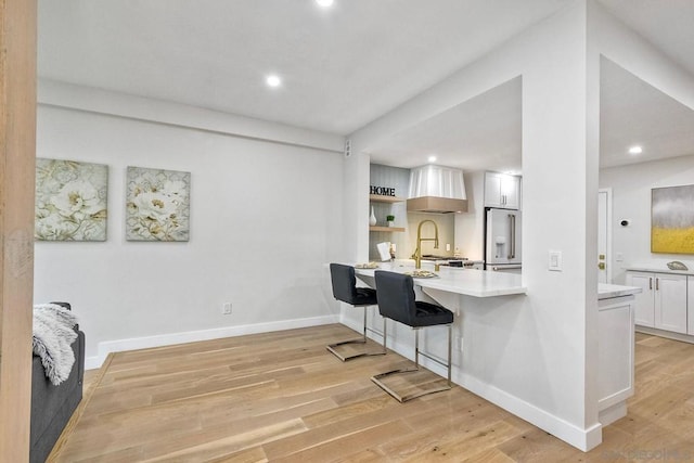 kitchen with white cabinetry, light hardwood / wood-style floors, high end fridge, and premium range hood