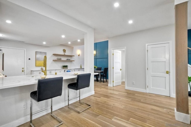 kitchen featuring light stone counters, a breakfast bar, kitchen peninsula, and light wood-type flooring