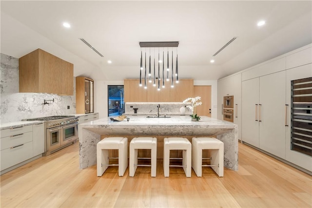 kitchen featuring decorative light fixtures, tasteful backsplash, an island with sink, double oven range, and light stone counters