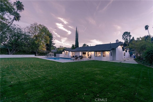 back house at dusk with a lawn and a patio