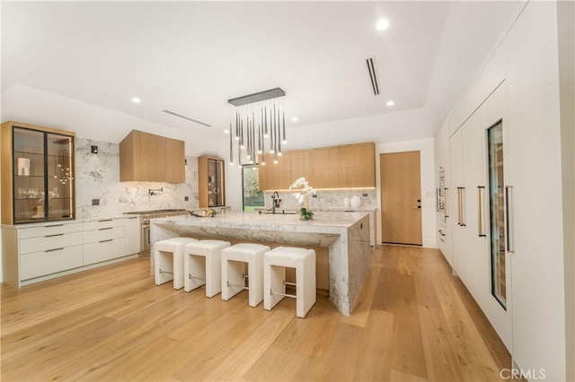 kitchen with a center island, white cabinetry, tasteful backsplash, light hardwood / wood-style floors, and light stone counters