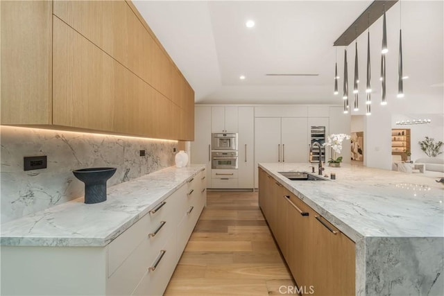 kitchen with decorative backsplash, sink, hanging light fixtures, light brown cabinetry, and light wood-type flooring