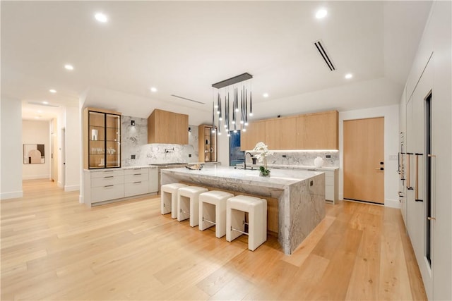 kitchen featuring light stone counters, white cabinetry, decorative backsplash, and a kitchen island with sink