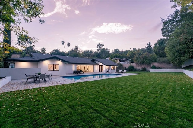 pool at dusk featuring a patio area and a lawn