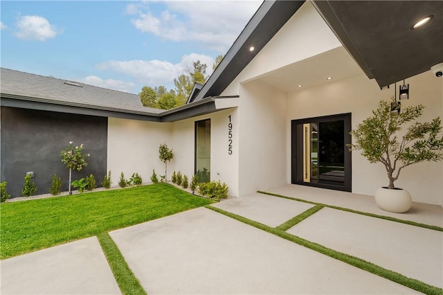 entrance to property featuring a lawn and a patio