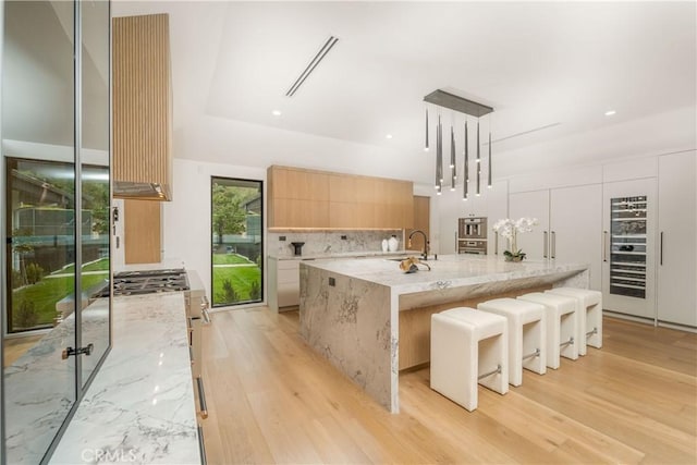 kitchen featuring light hardwood / wood-style floors, light stone countertops, a large island with sink, and hanging light fixtures