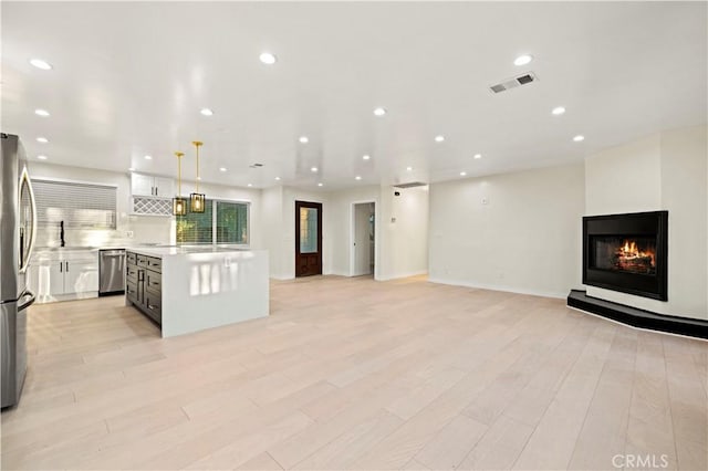 kitchen featuring pendant lighting, appliances with stainless steel finishes, a kitchen island, a multi sided fireplace, and light wood-type flooring