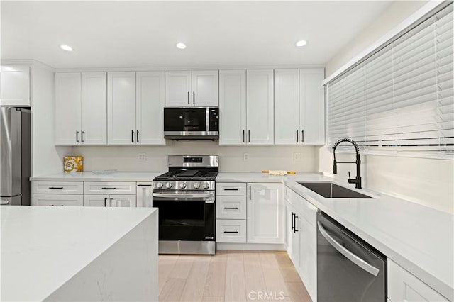 kitchen with appliances with stainless steel finishes, sink, white cabinetry, and light hardwood / wood-style flooring