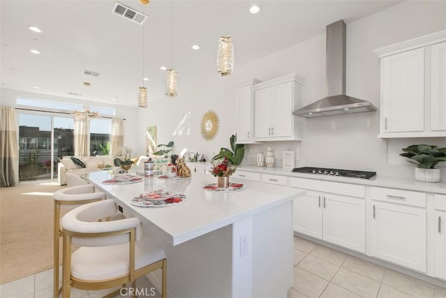 kitchen with pendant lighting, wall chimney range hood, white cabinetry, an island with sink, and a breakfast bar area