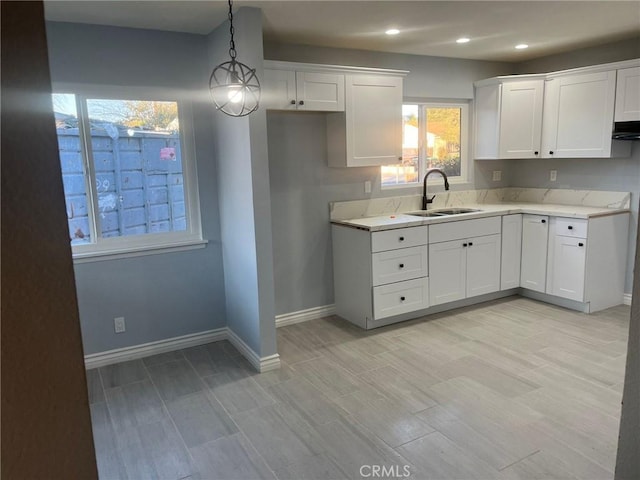 kitchen featuring white cabinets, pendant lighting, light stone counters, and sink