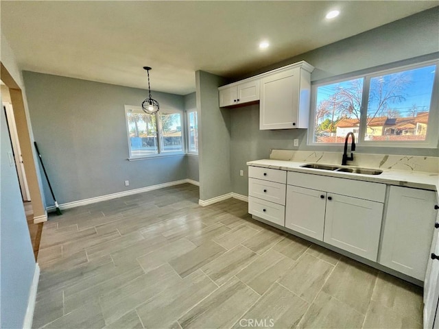 kitchen featuring white cabinetry, sink, light stone countertops, a chandelier, and pendant lighting