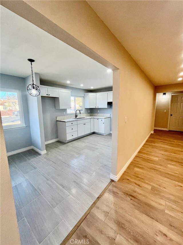 kitchen featuring white cabinets, decorative light fixtures, light wood-type flooring, and sink