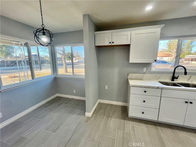 kitchen with light stone counters, sink, white cabinets, and decorative light fixtures