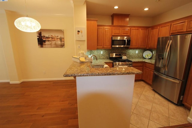 kitchen with kitchen peninsula, hanging light fixtures, stainless steel appliances, light stone counters, and a chandelier