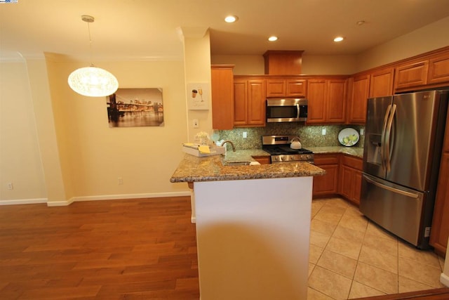 kitchen with kitchen peninsula, a breakfast bar area, appliances with stainless steel finishes, light stone countertops, and pendant lighting