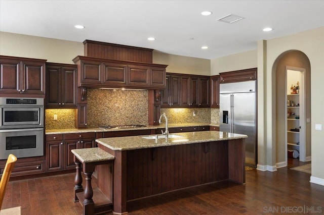 kitchen with a center island with sink, sink, light stone countertops, a kitchen breakfast bar, and stainless steel appliances