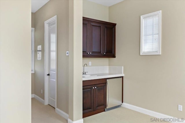 bar with sink, light colored carpet, dark brown cabinetry, and refrigerator