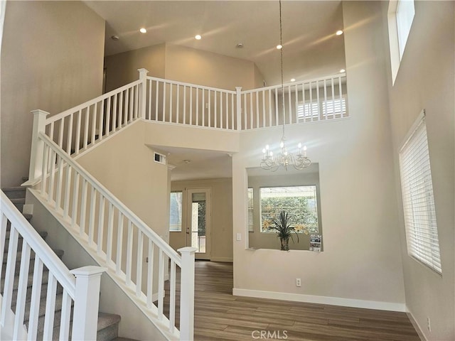 stairs featuring wood-type flooring, a towering ceiling, and an inviting chandelier