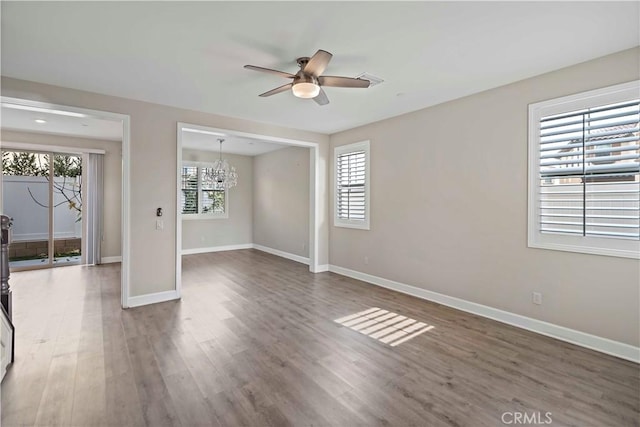 spare room featuring a wealth of natural light, ceiling fan with notable chandelier, and dark hardwood / wood-style flooring