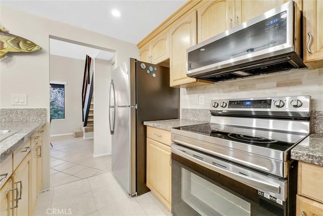 kitchen featuring light brown cabinetry, light tile patterned floors, appliances with stainless steel finishes, and stone counters