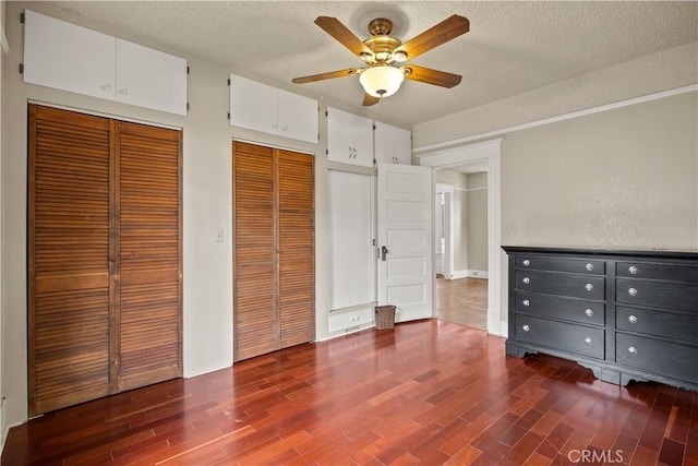 unfurnished bedroom with dark wood-style floors, a textured ceiling, and two closets