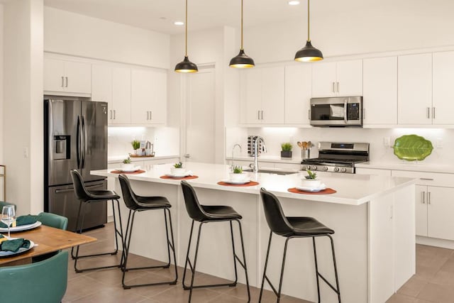 kitchen with a center island with sink, stainless steel appliances, and white cabinetry