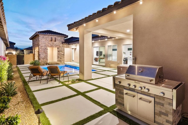 patio terrace at dusk featuring exterior kitchen and a fenced in pool