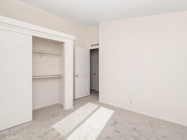 unfurnished bedroom with light colored carpet, a textured ceiling, and a closet